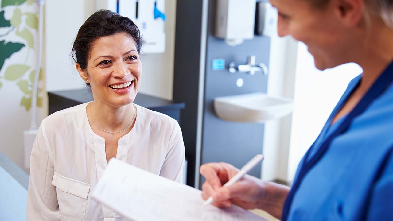 female patient at the clinic sitting on exam table with nurse holding clipboard. they are discussion the weight loss program